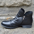 Black leather ankle boot shown from the side, featuring a low stacked heel and dual side zips.