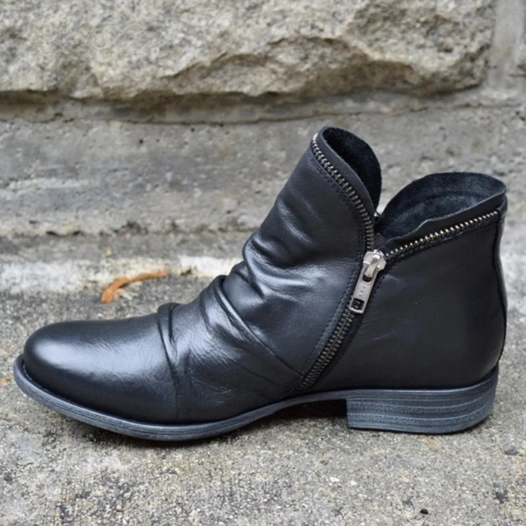 Black leather ankle boot shown from the side, featuring a low stacked heel and dual side zips.