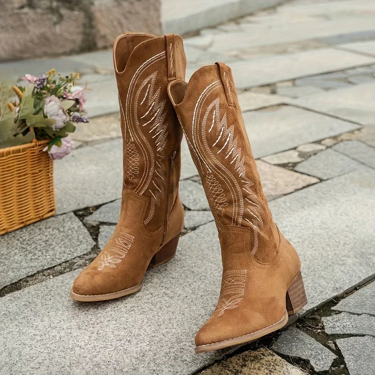Front angled view of a pair of brown embroidered cowboy boots with pointed toes standing on stone pavement.