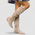 Side view of beige suede knee-high slouch boot with low block heel and ankle strap detail