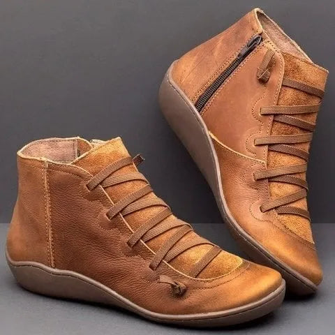 Pair of tan brown leather ankle boots with cross lacing and side zip, shown against a grey backdrop