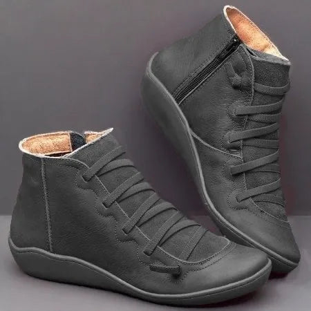 Black leather ankle boots with cross-laced front and matching black zip, shown on a dark backdrop
