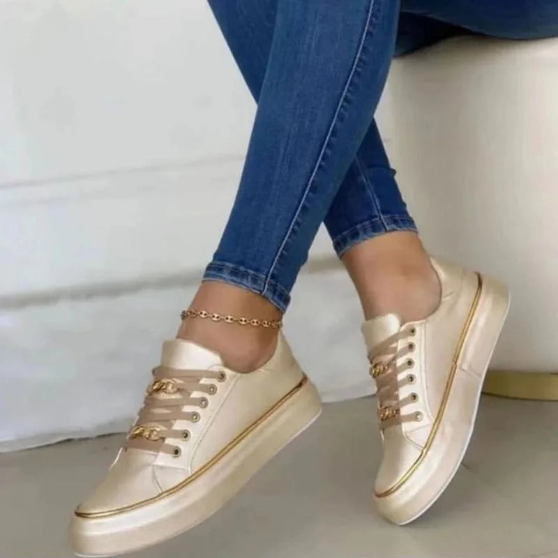 Gold-tone lace-up trainers with metallic finish and matching chain detail, worn seated with jeans