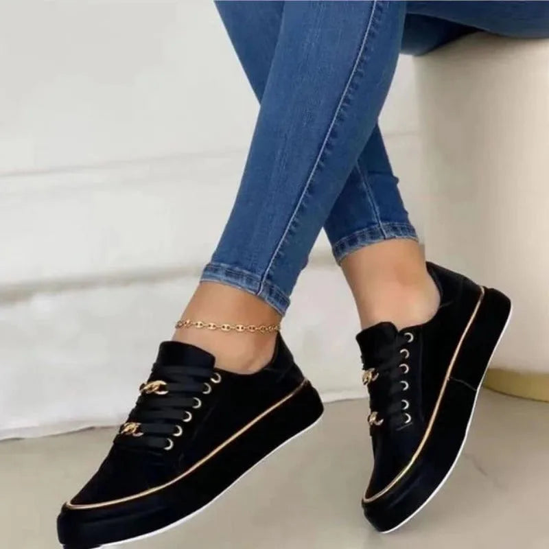 Black lace-up trainers with gold chain trim and white platform sole, side view worn while seated