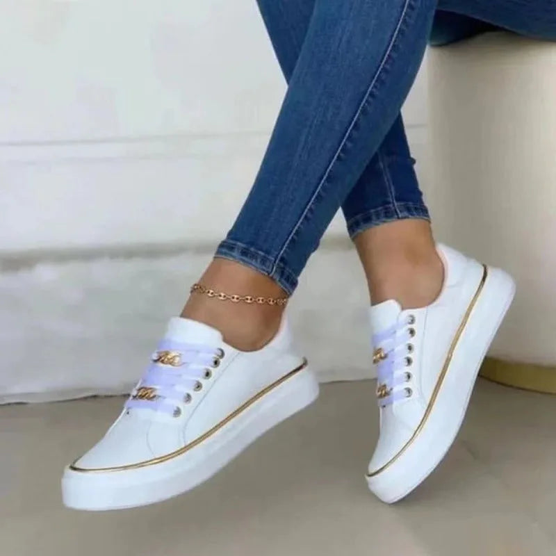 Close-up side view of white trainers with lilac laces, gold chain detail and gold trim on the sole
