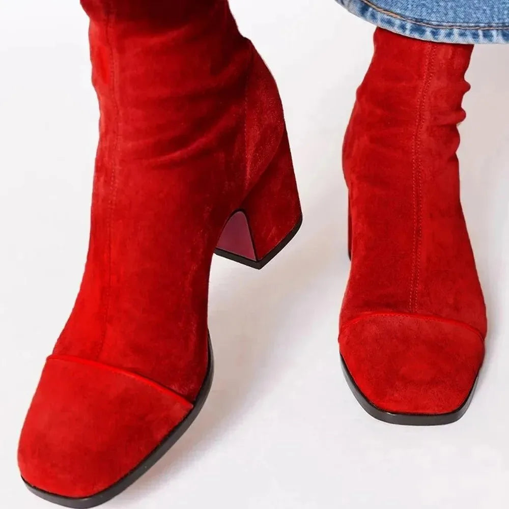 Red suede ankle boots with contrast toe cap and block heel, viewed from above while worn with denim