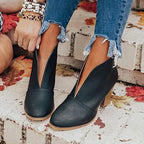 Black V-cut ankle boots with pointed toe and stacked heel, shown from the side against a stone step