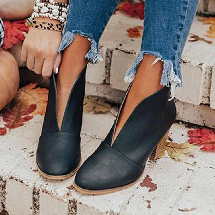 Black V-cut ankle boots with pointed toe and stacked heel, shown from the side against a stone step