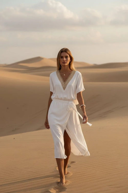 Front view of ivory wrap midi dress with tie belt and short sleeves, worn walking on sand.