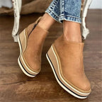 Side view of khaki suede wedge ankle boot with side zip and striped platform sole, worn with cuffed jeans