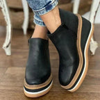 Front angle of black leather wedge ankle boot showing round toe and tan-edged platform sole