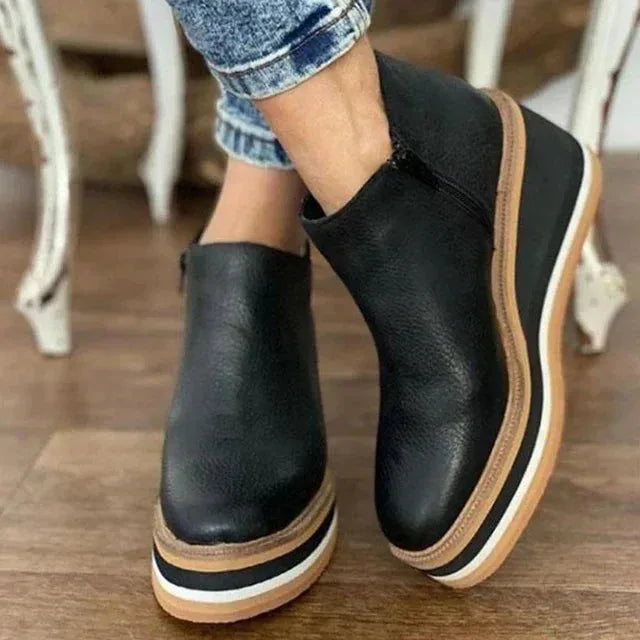 Front angle of black leather wedge ankle boot showing round toe and tan-edged platform sole