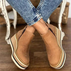 Crossed-ankle view of tan suede wedge boots highlighting the side zipper and layered platform heel