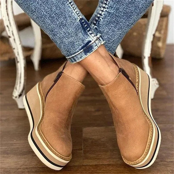 Crossed-ankle view of tan suede wedge boots highlighting the side zipper and layered platform heel