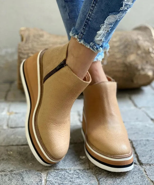 Close-up of beige leather wedge boot with contrast zip trim and cream-striped platform sole
