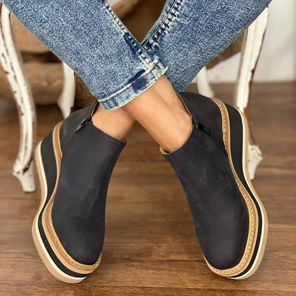 Side view of navy blue leather wedge ankle boot with tan platform sole against a gravel background